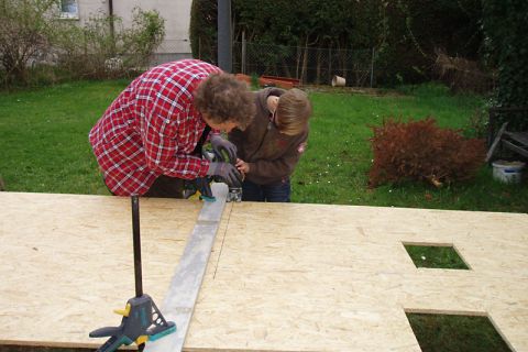Betreuer und Junge beim Aussägen einer Holzplatte