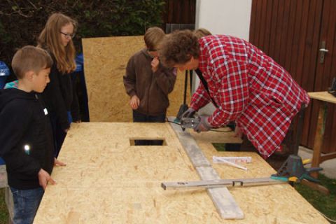 Betreuer und Kindergruppe beim Aussägen von Öffnungen aus einer Holzplatte