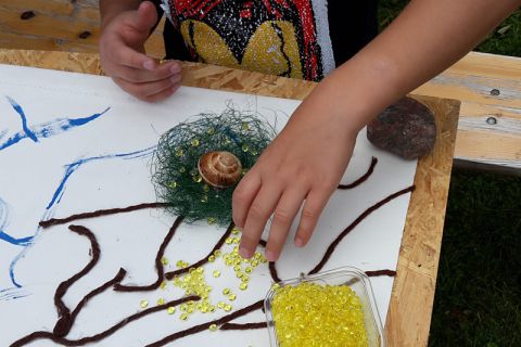 Kind platziert gelbe Steine auf Lebensbaum
