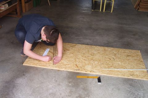 Junge beim Aufzeichnen der benötigten Form auf die Holzplatte